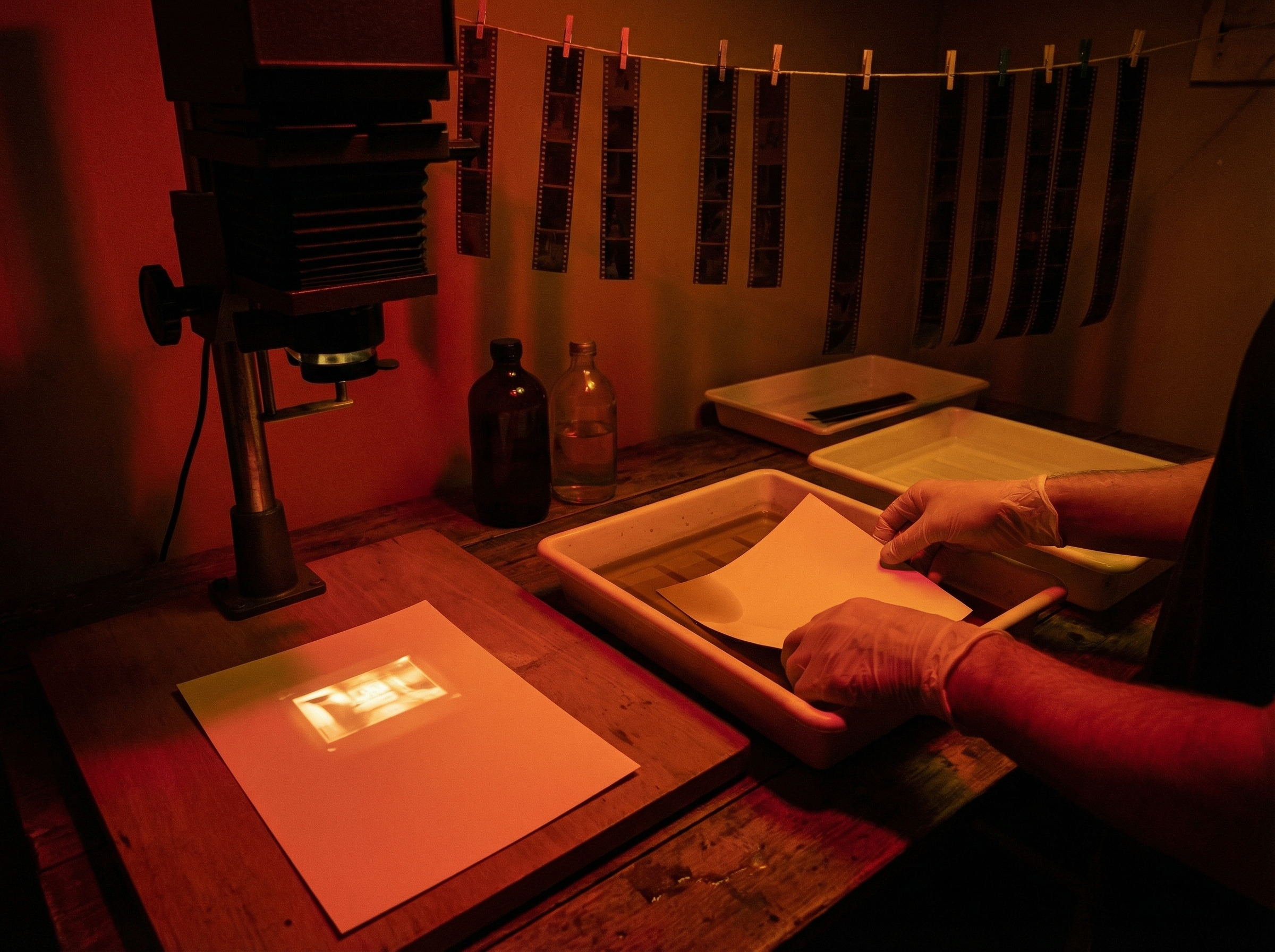 Hands working in a photography darkroom, chemical trays and enlarger casting dramatic light