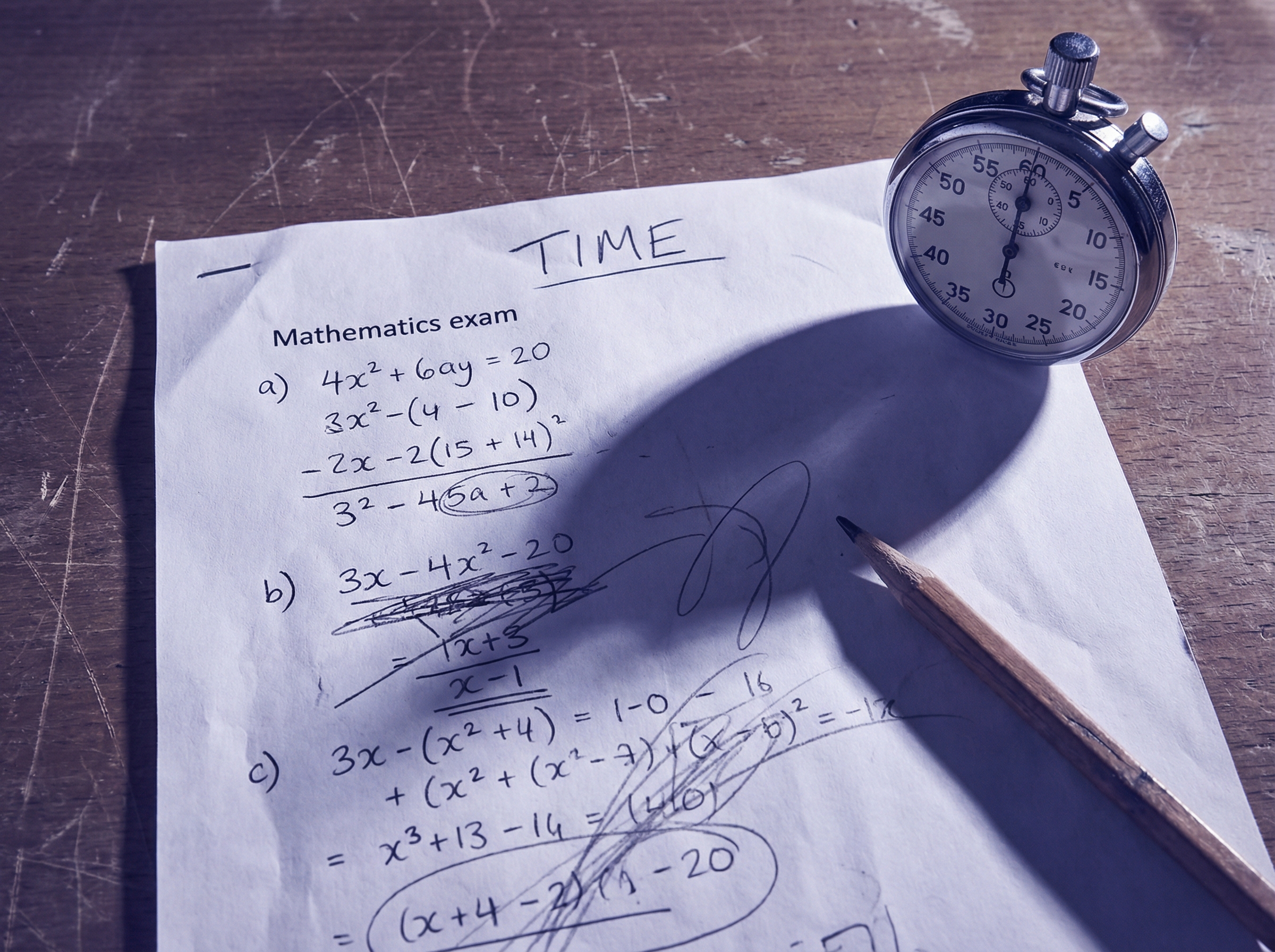 Close-up of a handwritten mathematics exam paper on a wooden desk with a stopwatch beside it