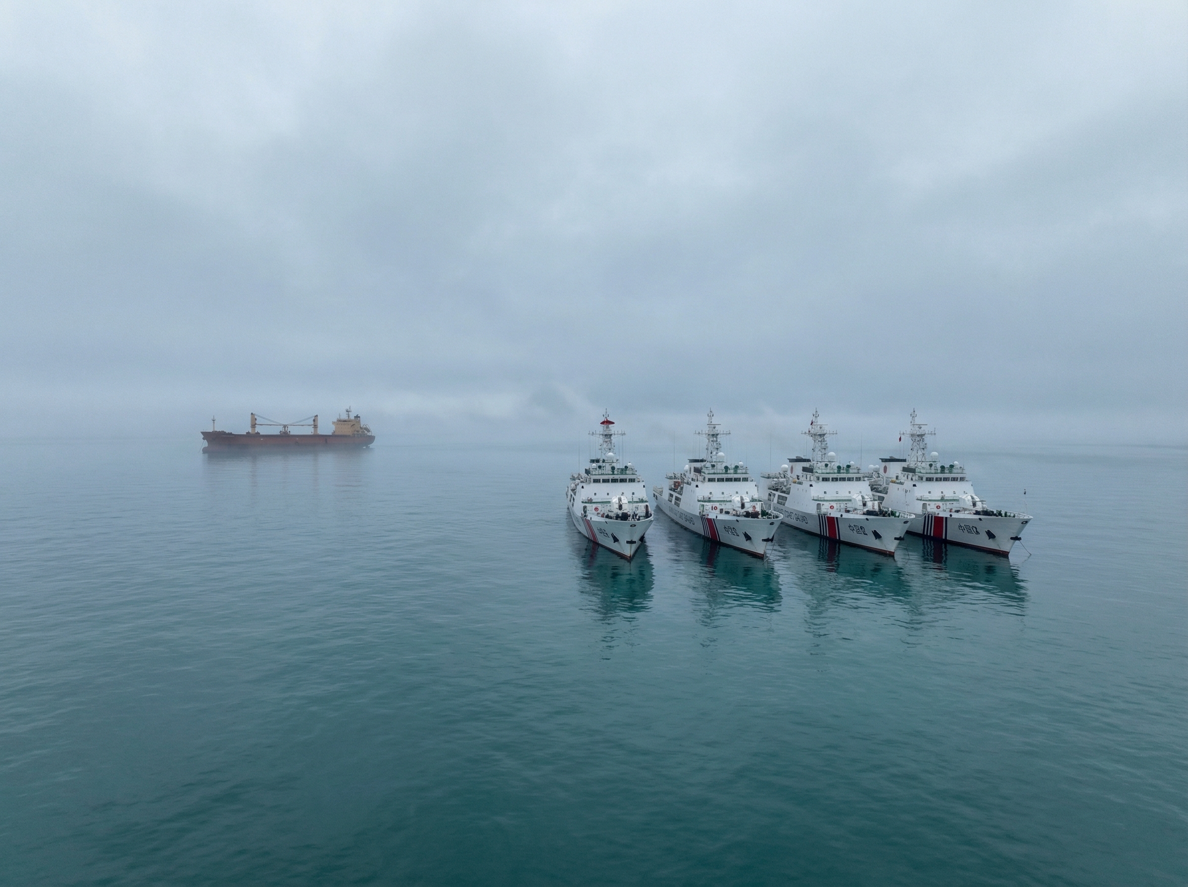 Chinese coast guard vessels forming a line across ocean waters with cargo ship waiting in distance
