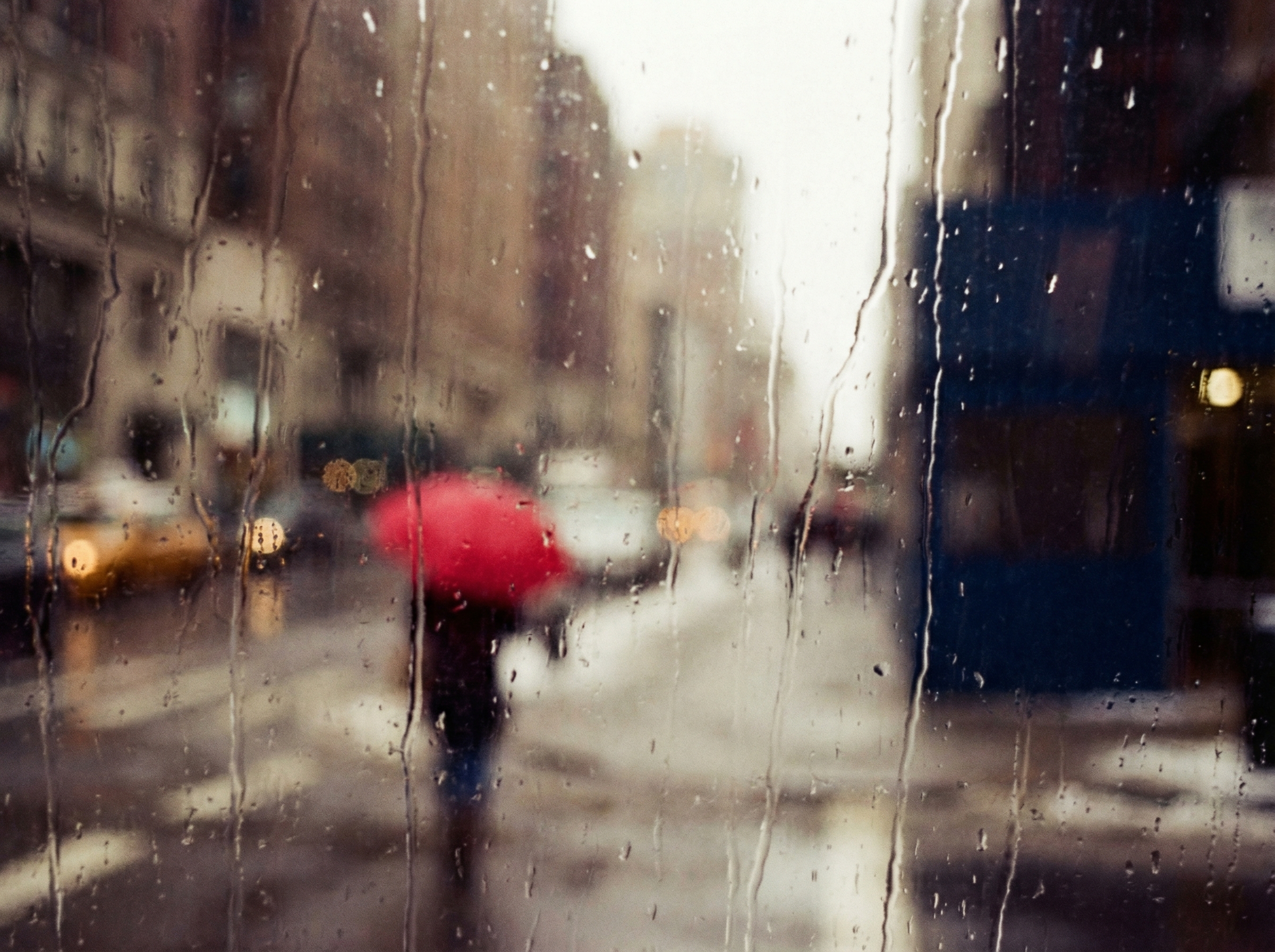 An abstract painterly street scene through rain-streaked window with vibrant red umbrella
