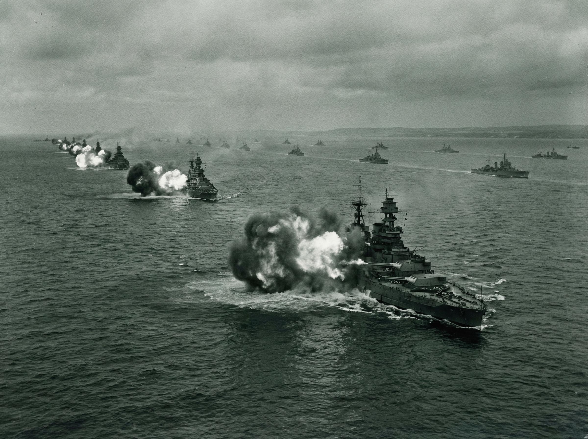 WWII battleships firing broadside toward shore with massive muzzle flashes