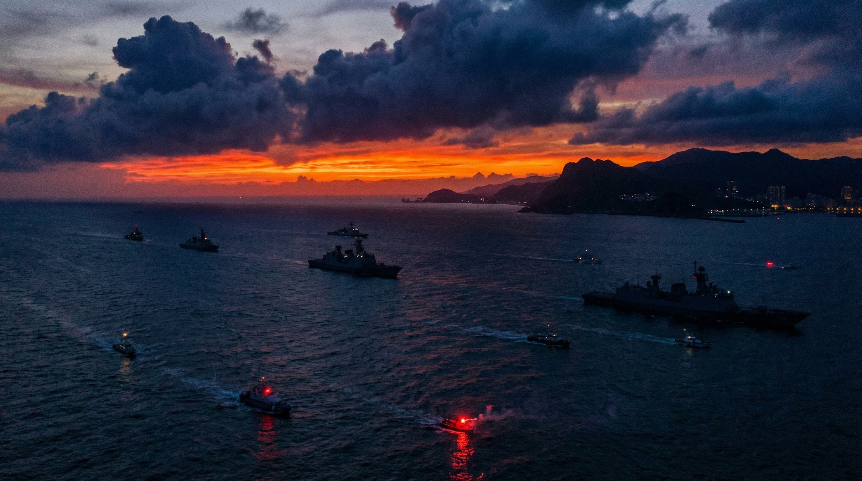 Taiwan Strait at dusk with military vessels silhouetted against a dramatic sky